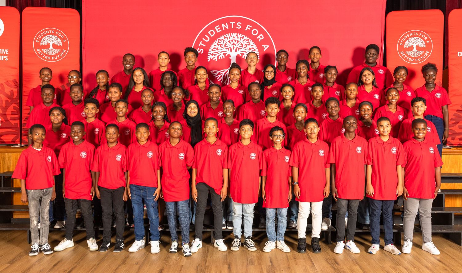 Large group of students in red uniforms posing together against a red backdrop.