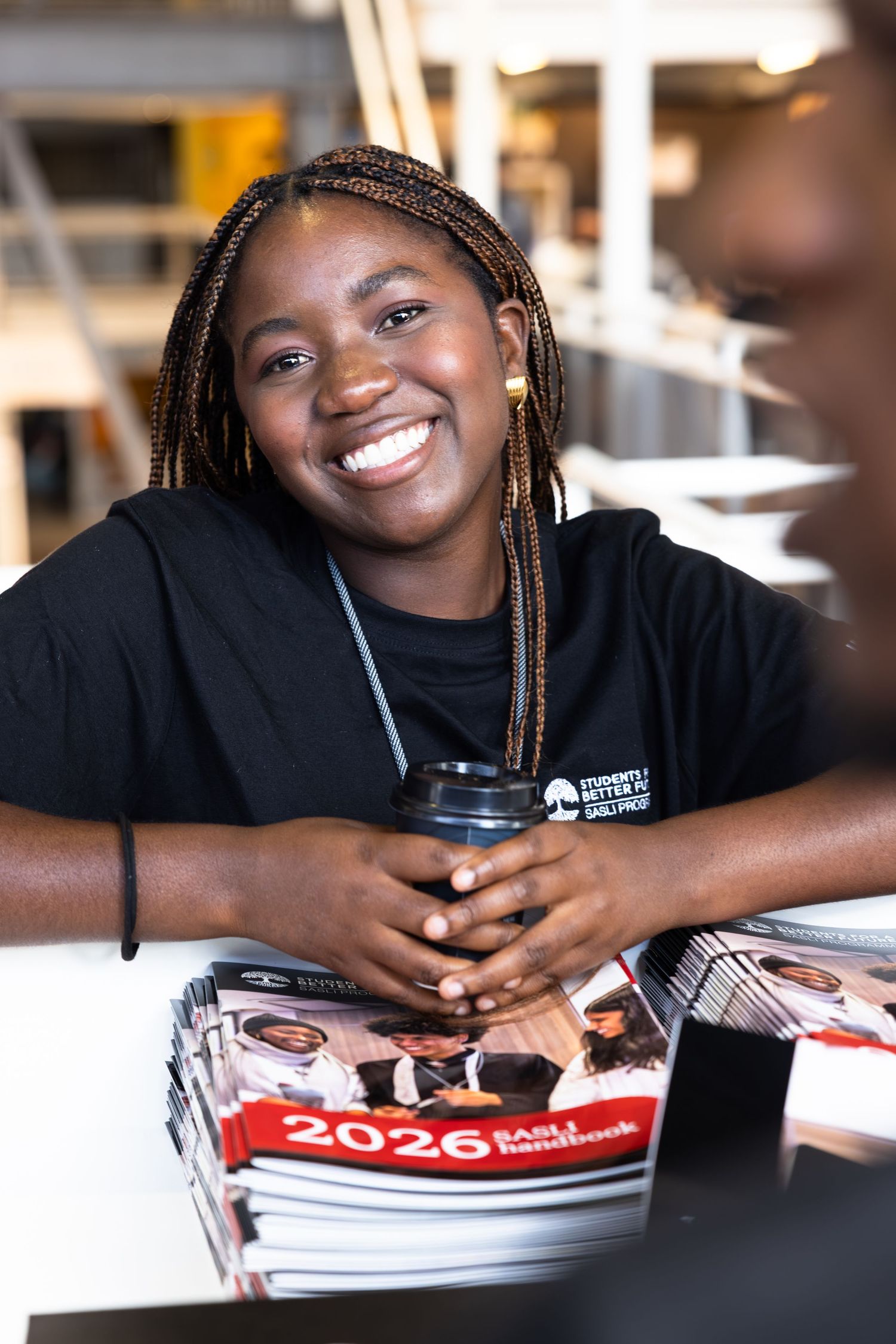 Staff member in black shirt smiles while holding a drink during event registration.