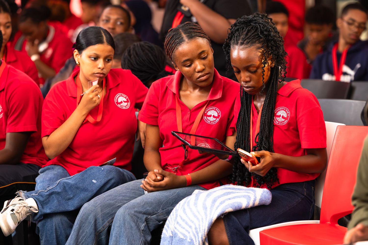 Attendees in red shirts seated and engaged during conference presentation.