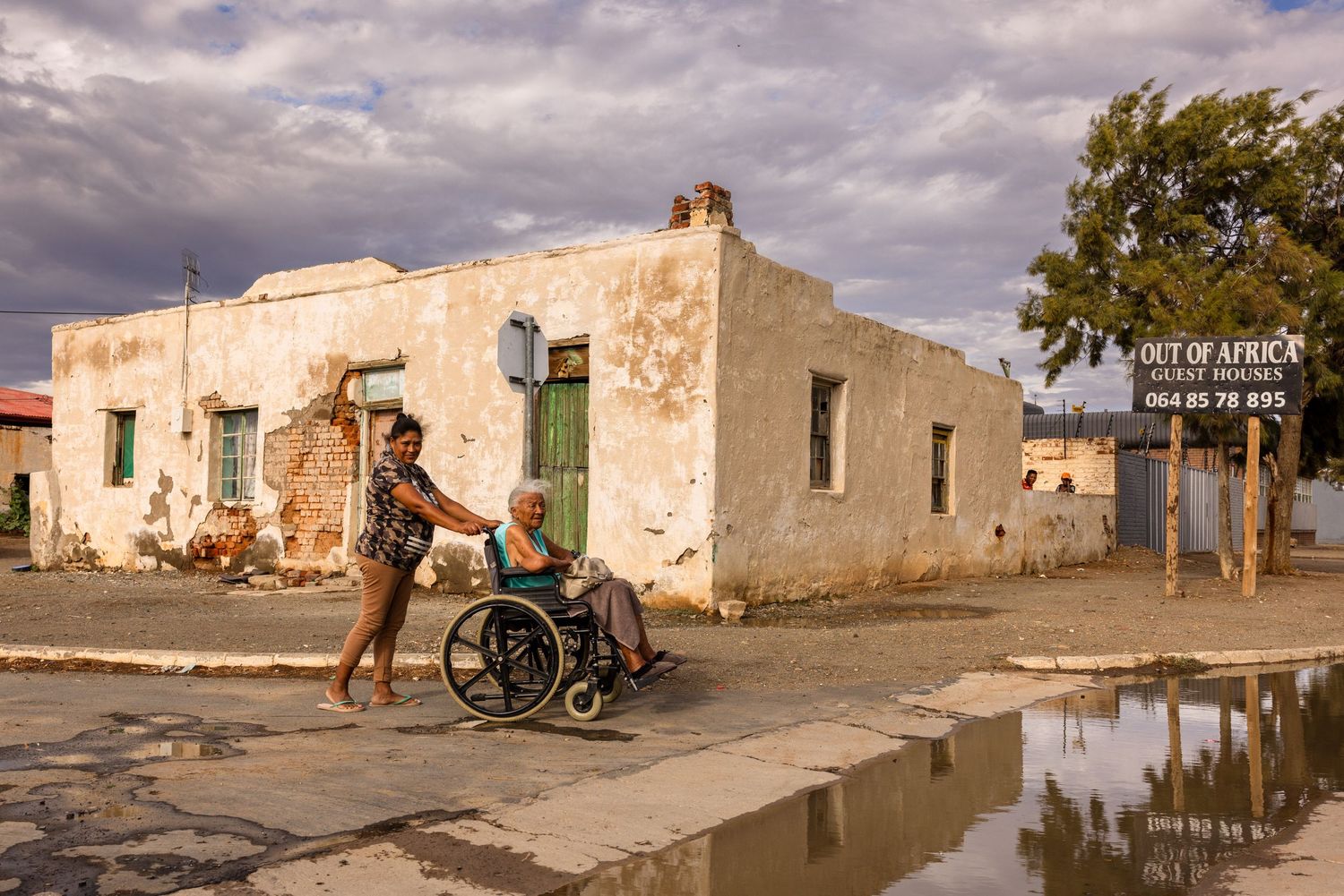 Row of weathered white buildings with green doors along a flooded street in a rural setting.