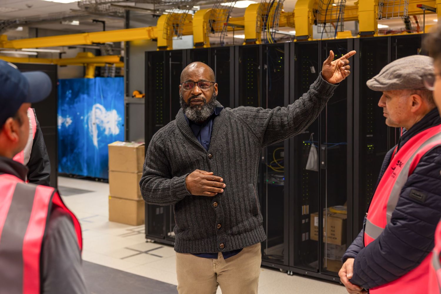 Discussion taking place in data center with rows of yellow server racks visible.