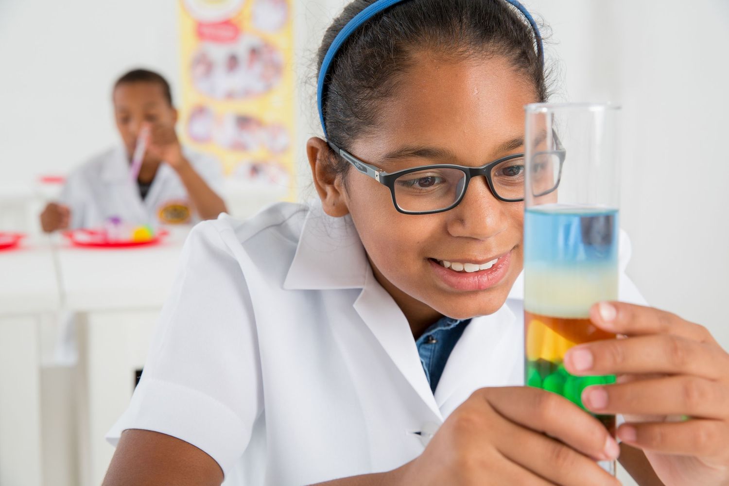 Student in lab coat examining colorful liquid samples in science class laboratory setting.
