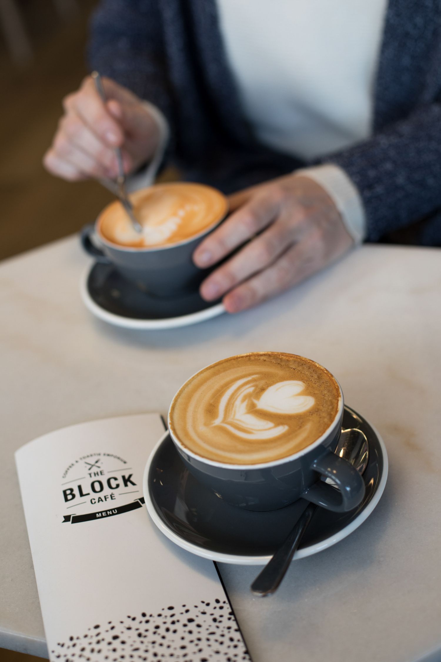 Artistically crafted latte art in dark ceramic cups on a cafe counter.