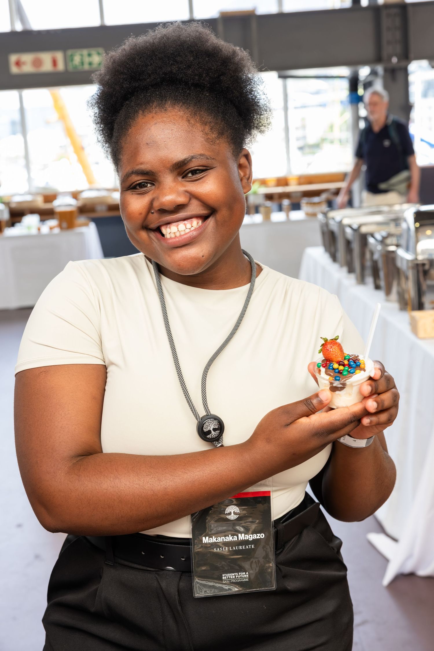 Person in a white shirt and black apron holding food items at a dining event.