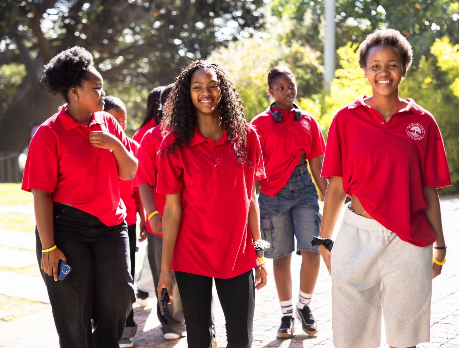 Students in red polo shirts walk together outdoors on a sunny day.