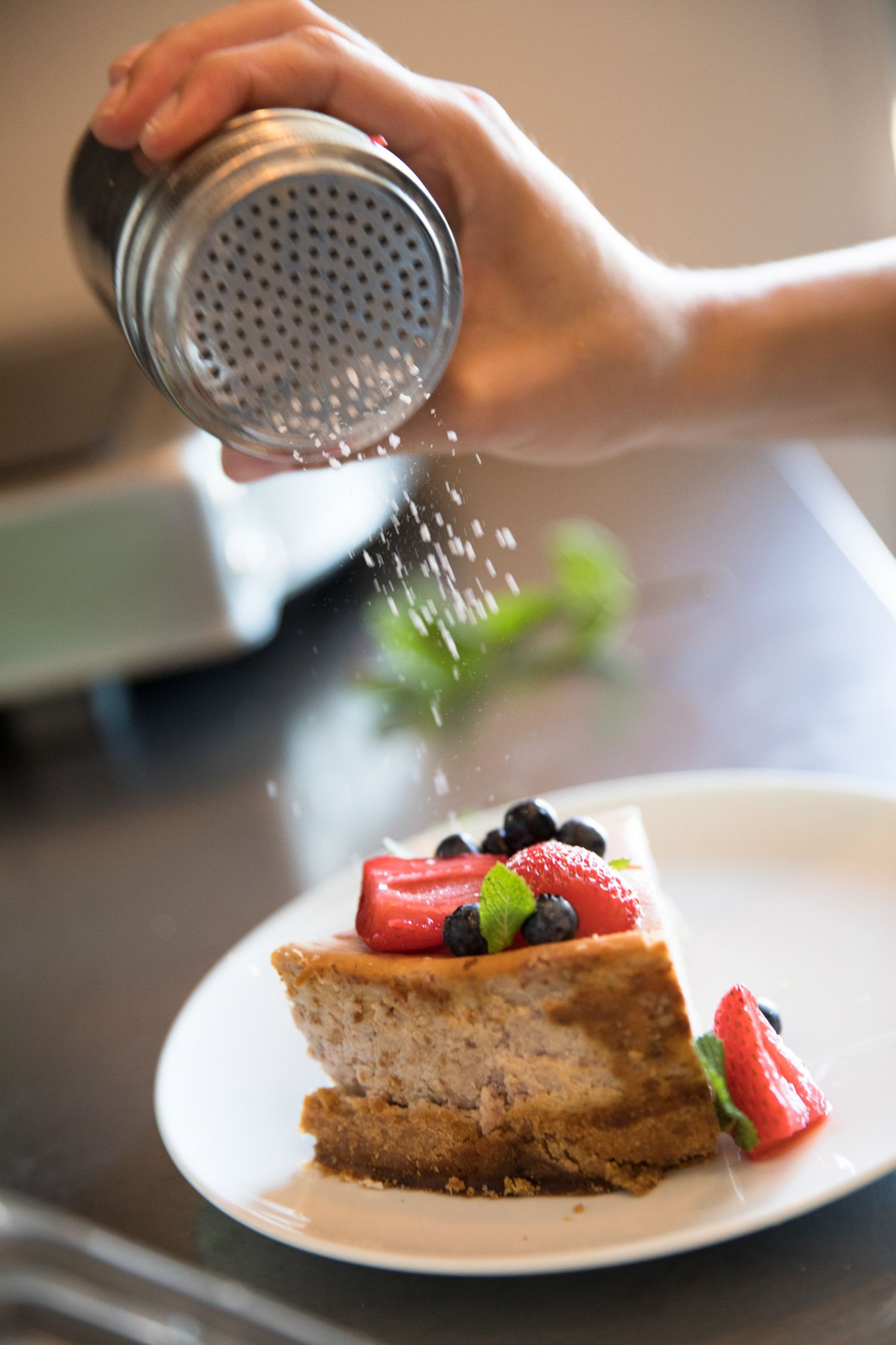 Powdered sugar being sprinkled over a slice of cake topped with fresh berries.