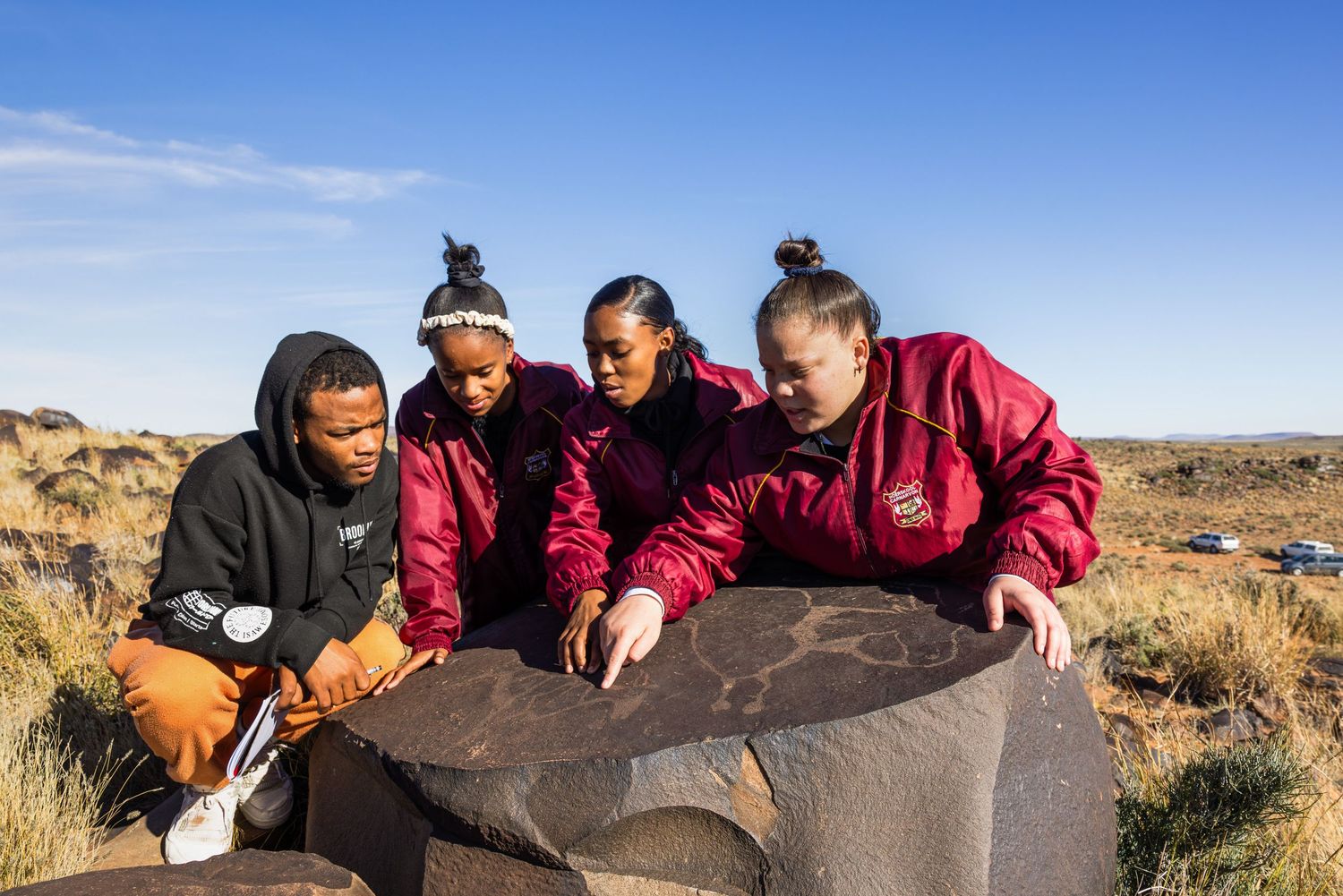 Group examining a large rock formation in an arid desert landscape.