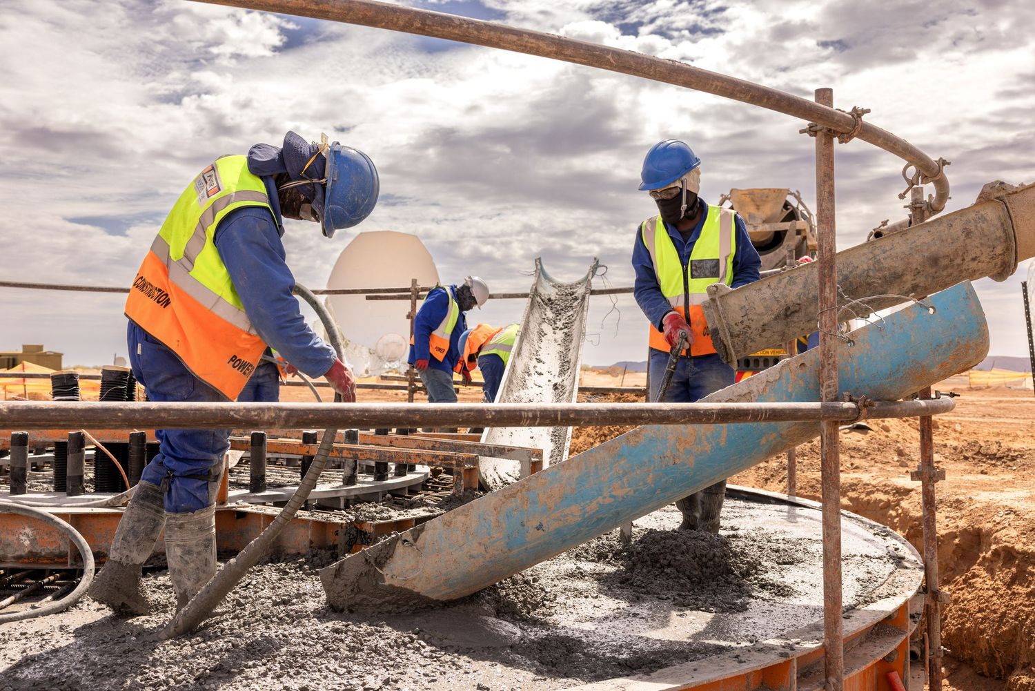 Workers pour and spread concrete at construction site with wooden formwork.