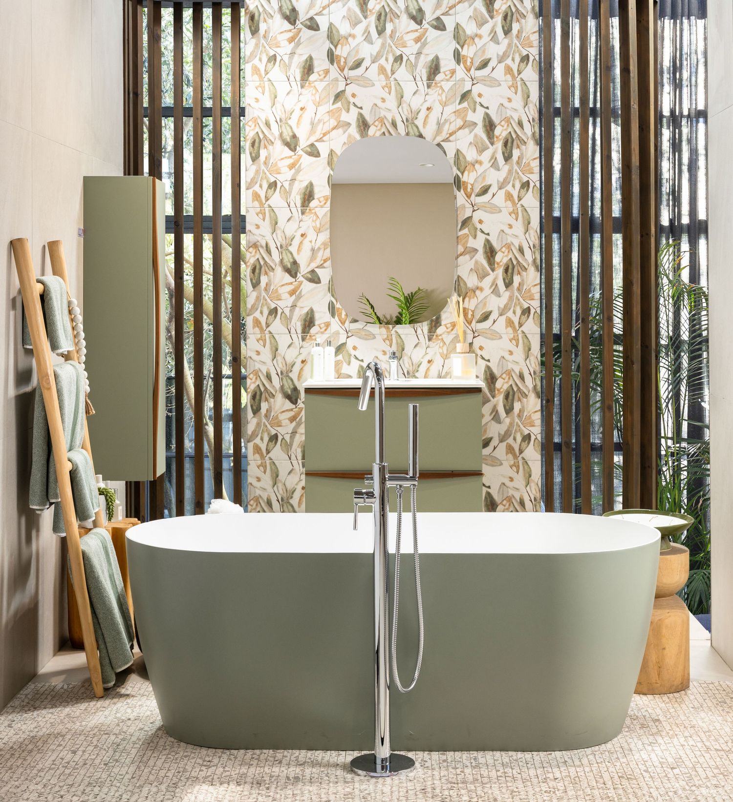 Contemporary bathroom featuring sage green freestanding tub against floral wallpaper with wooden slat dividers.