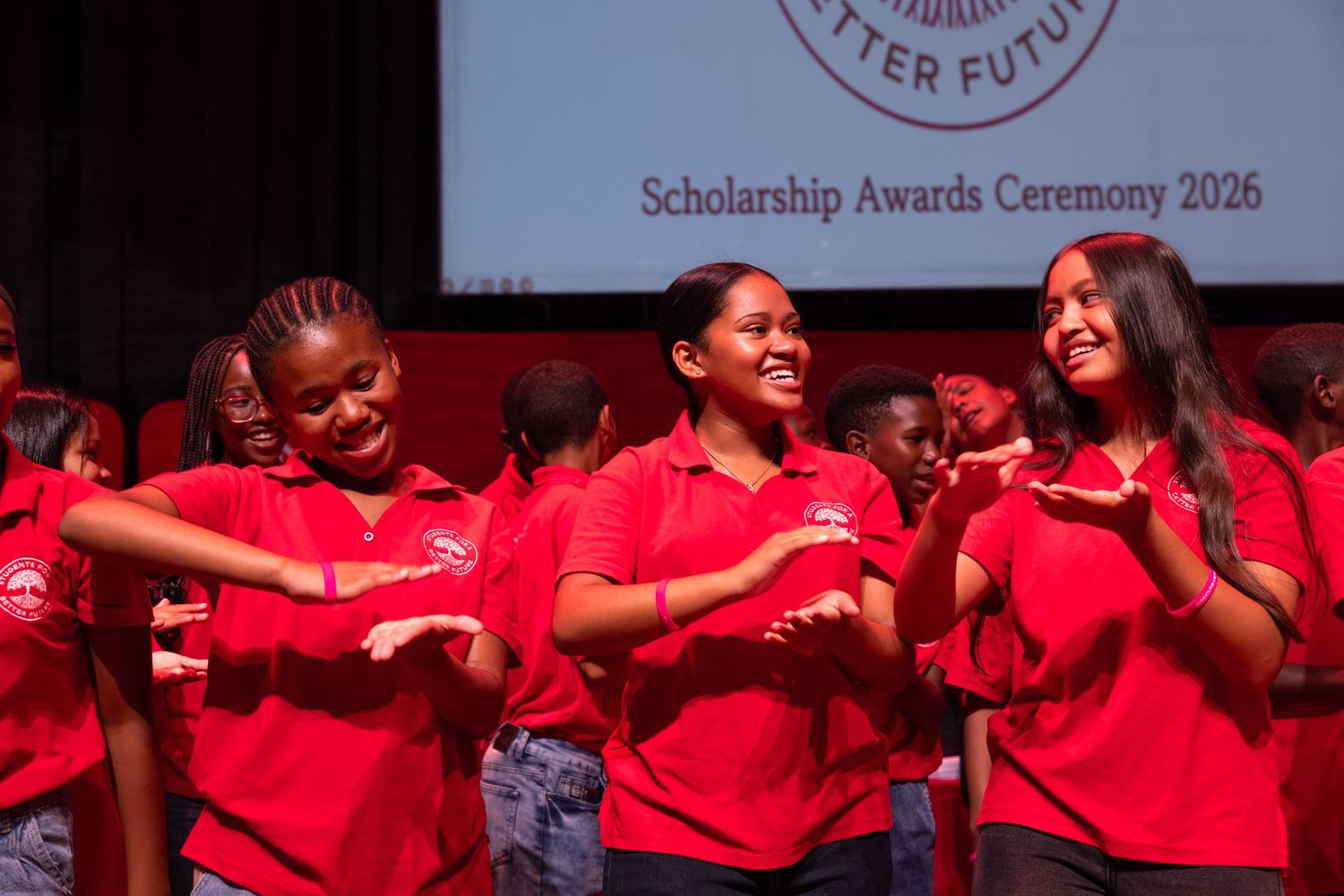 A group of students in red shirts celebrate during a scholarship awards ceremony.