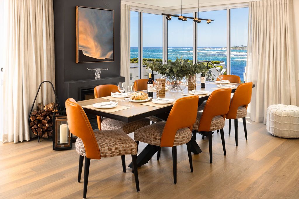 Luxurious oceanfront condo interior with orange dining chairs and panoramic views of the beach through floor-to-ceiling windows.