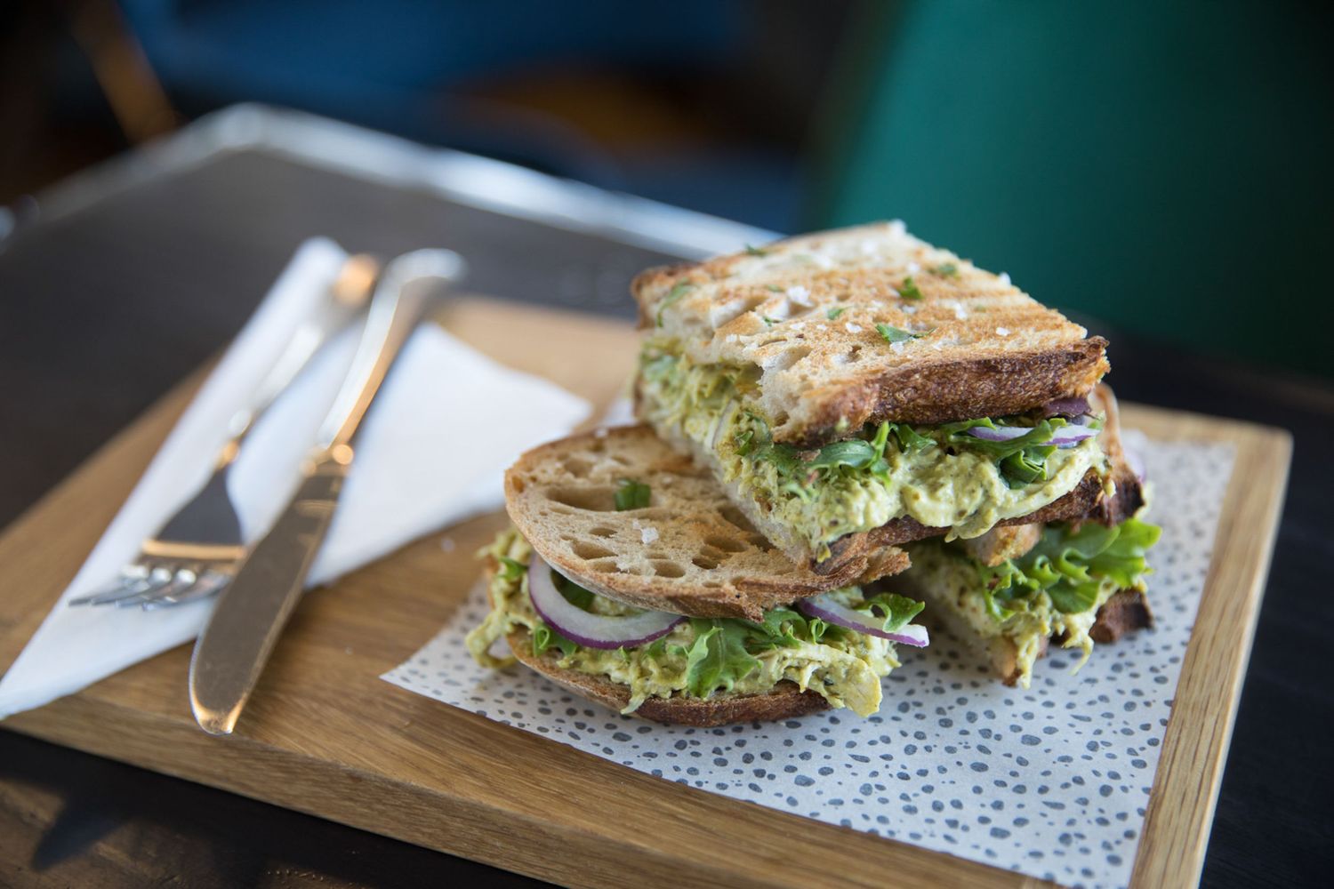 Fresh sandwiches with green lettuce served on wooden boards at a casual dining establishment.