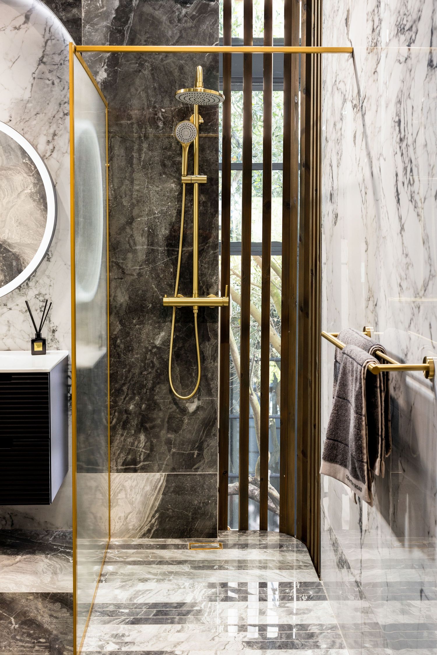 Contemporary bathroom interior with gold-framed shower enclosure and marble walls creating a spa-like atmosphere.