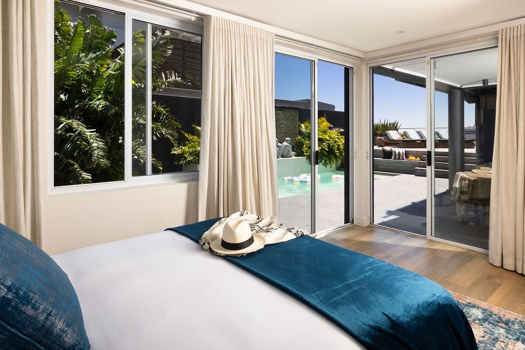 Luxurious bedroom with sliding glass doors opening to a pool area, featuring blue bedding and white curtains.