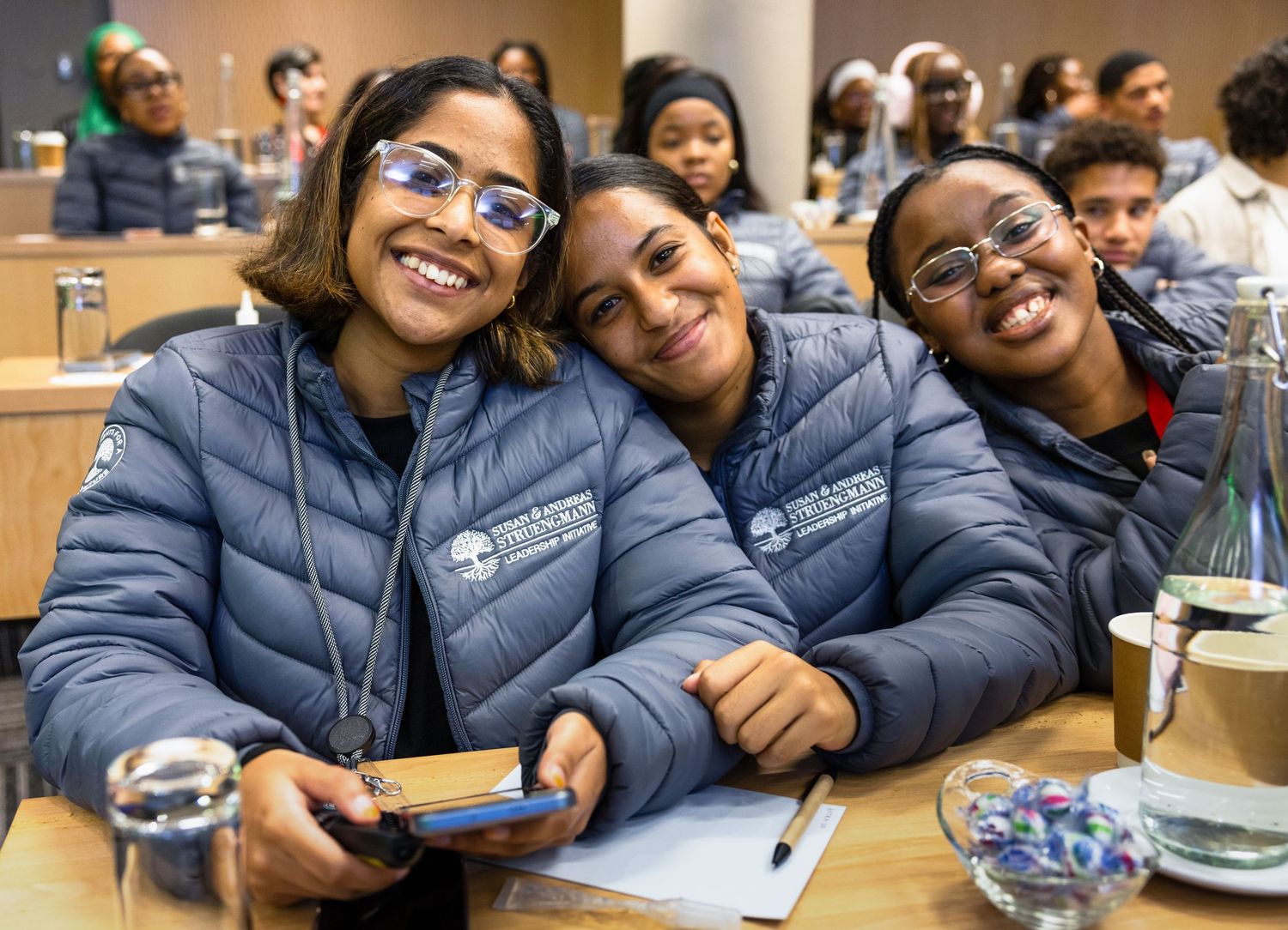 Students wearing matching blue puffer jackets smiling together during a study session.