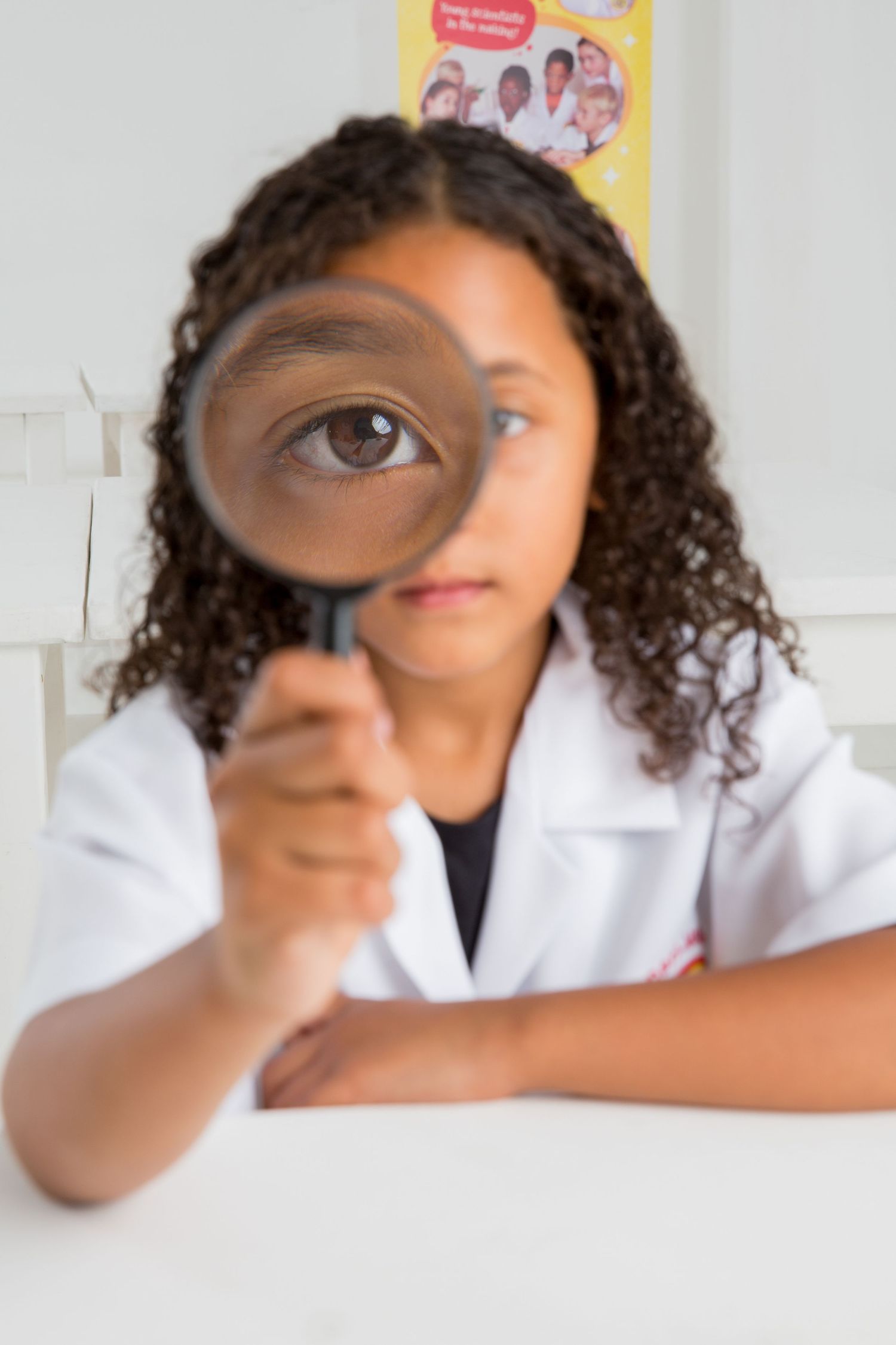 Young scientist in a white lab coat looks through magnifying glass during experiment.