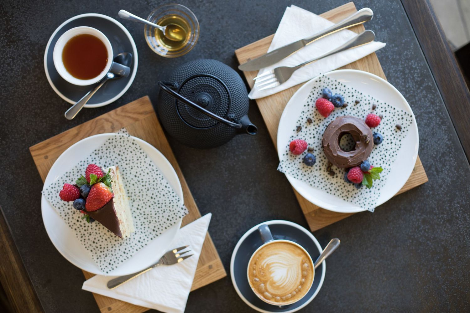 Overhead view of cafe table with various desserts, coffee cups, and wooden serving boards.