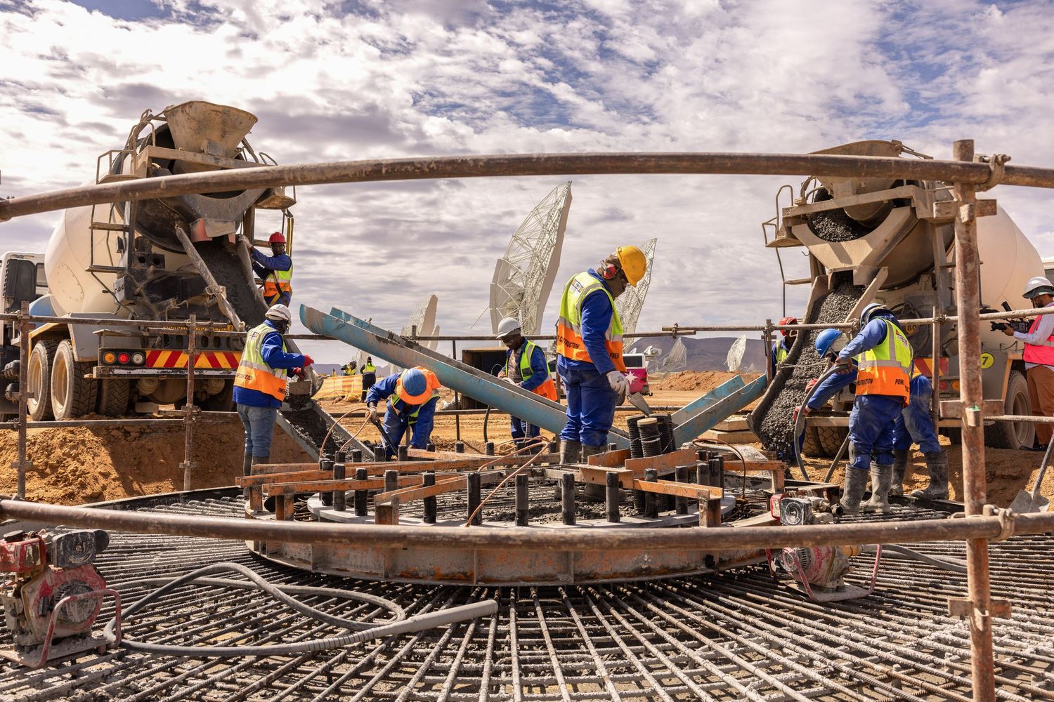 Construction crew working on concrete foundation with machinery at telescope facility site.
