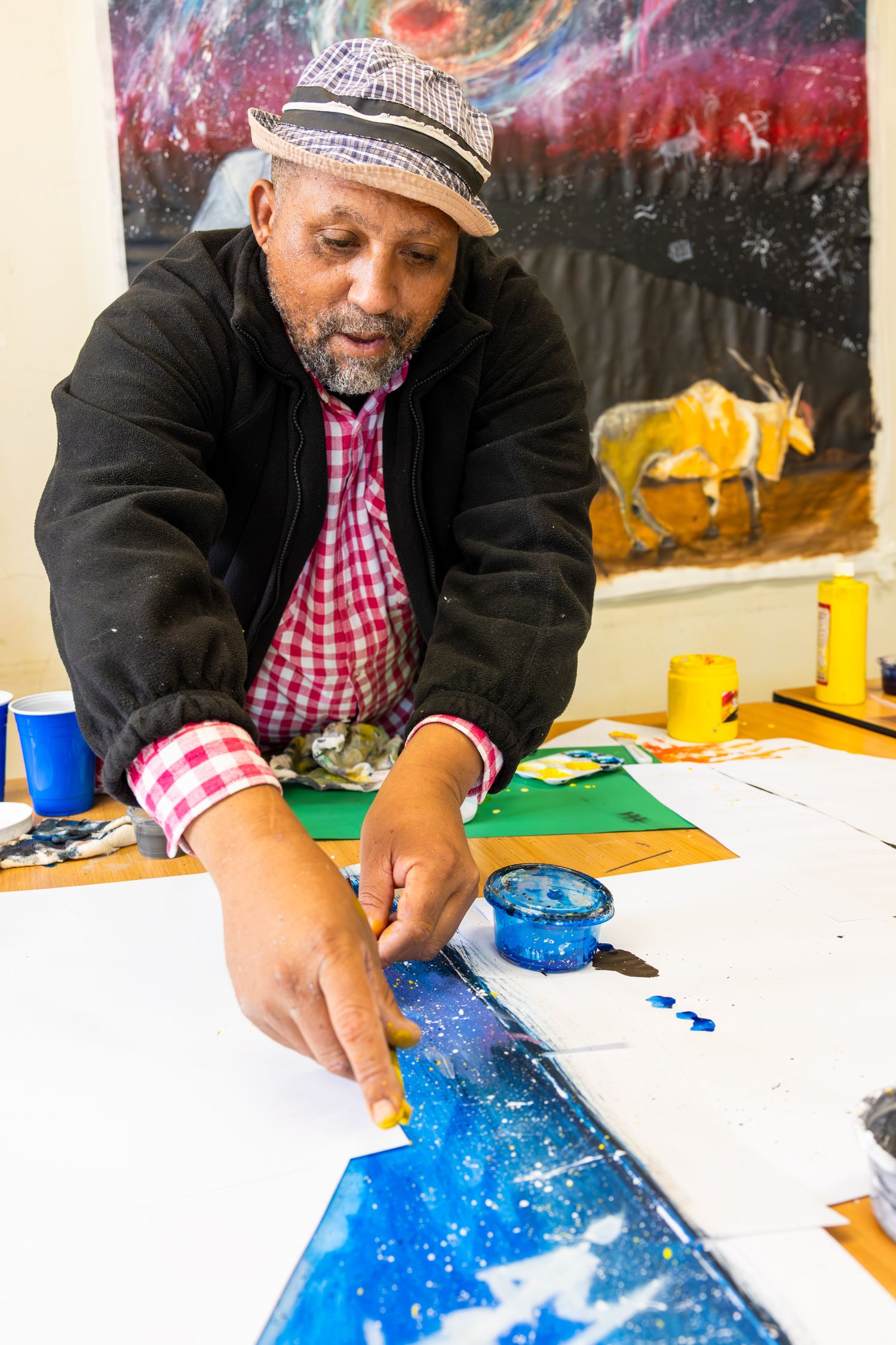 Artist working on a detailed blue painting against a cosmic-themed backdrop.