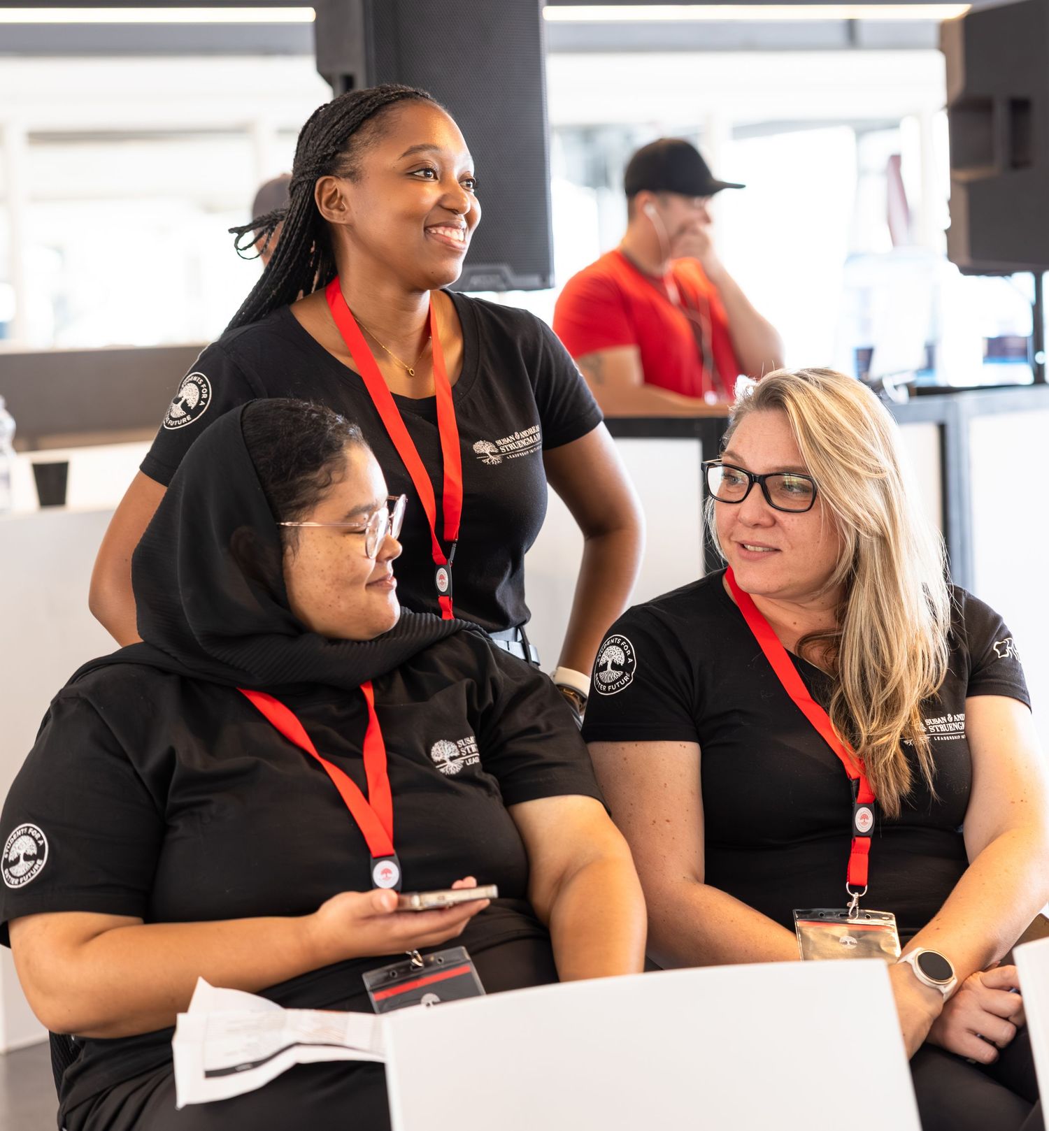 Team members in matching black uniforms and red lanyards collaborate while looking at a laptop during a meeting.