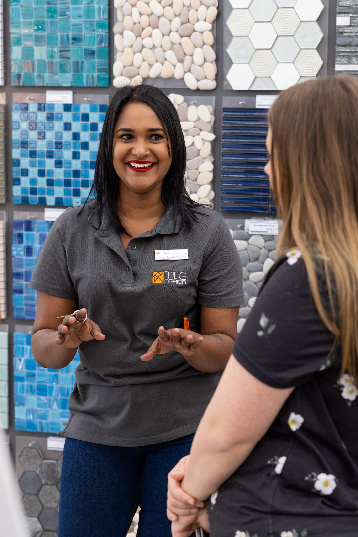 Staff member at a design shop showing tile samples in front of a mosaic wall display.