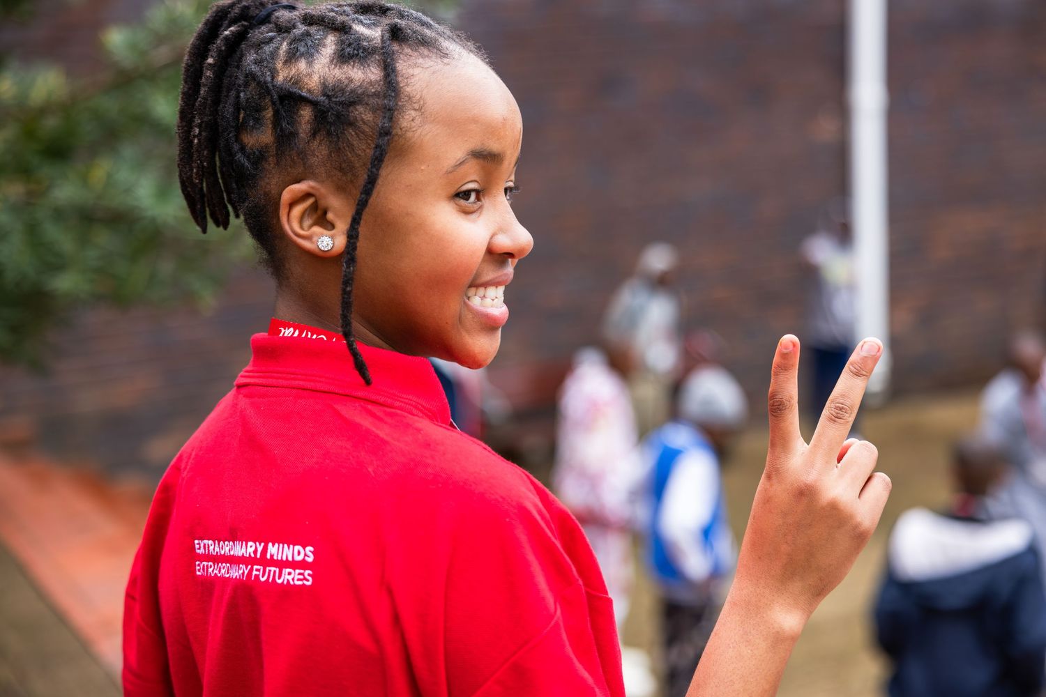 Staff member in red polo shirt gesturing peace sign outdoors.