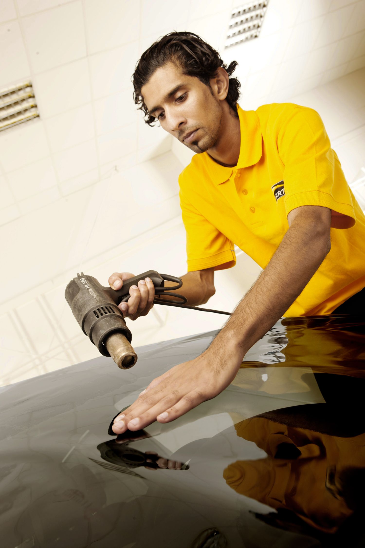 Auto detailer using power tool on dark vehicle surface during professional service.