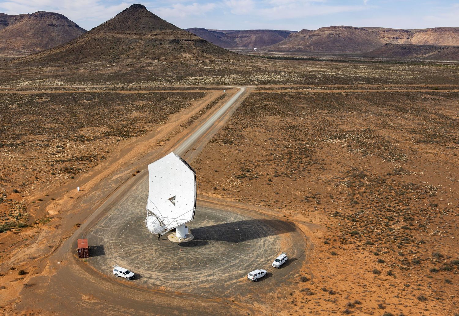 Aerial view of large satellite dish installation in desert with access road and vehicles.