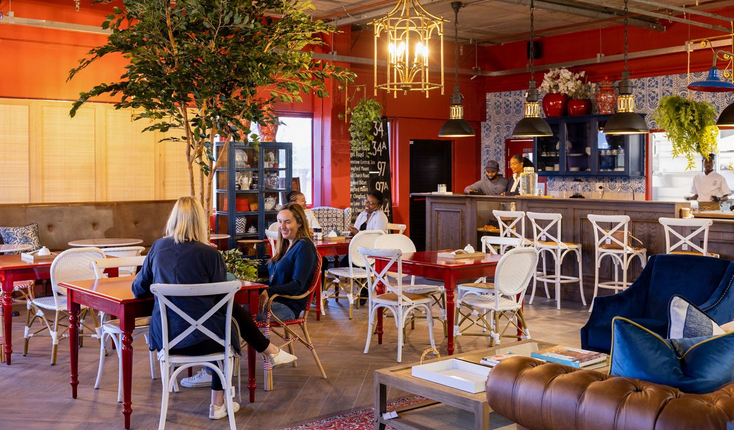 A modern restaurant space with red walls, hanging plants and white chairs.