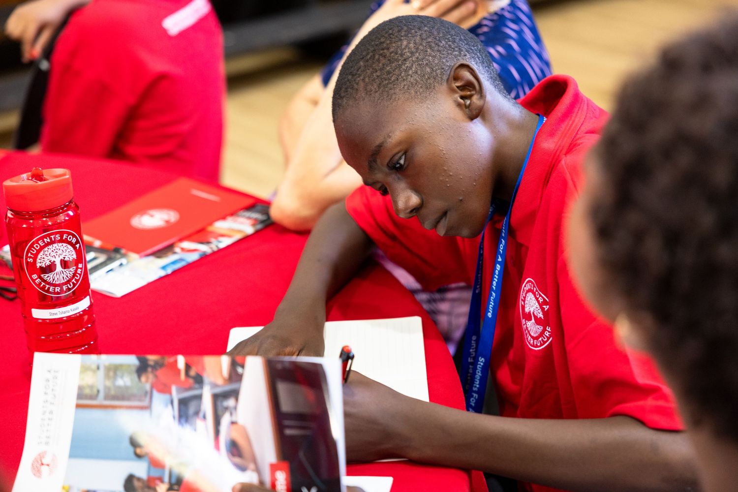 Students in red shirts working on an educational activity at tables.