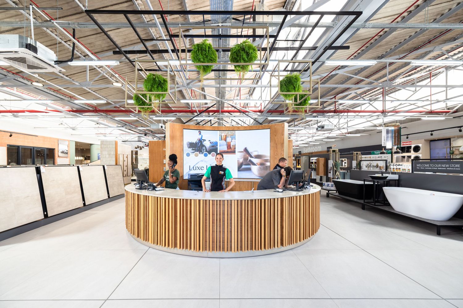 Modern open office space with industrial ceiling, wooden accents, and hanging plants creating a bright collaborative environment.