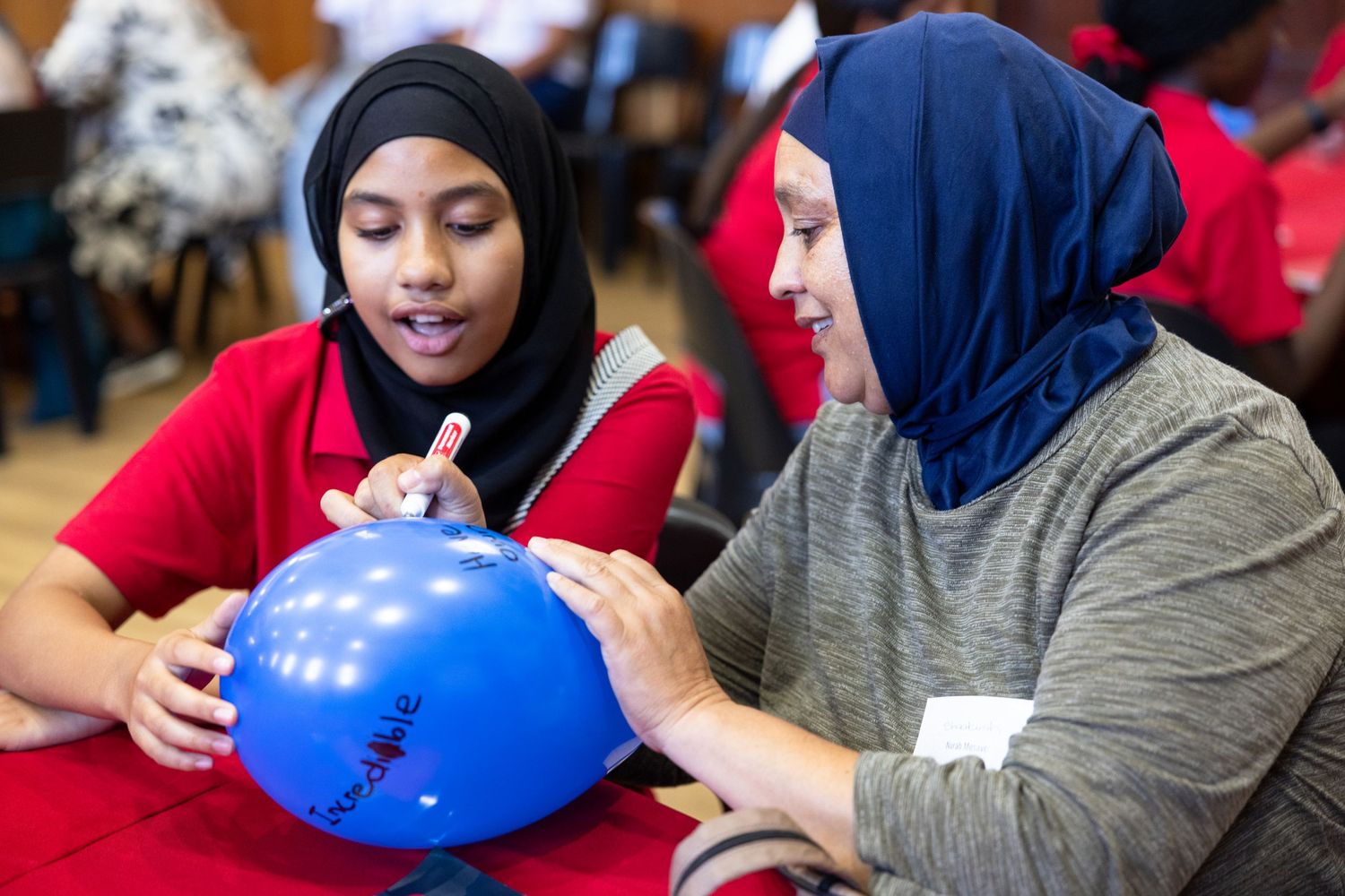 Several people in hijabs and baseball caps examine blue helmets at a community event.