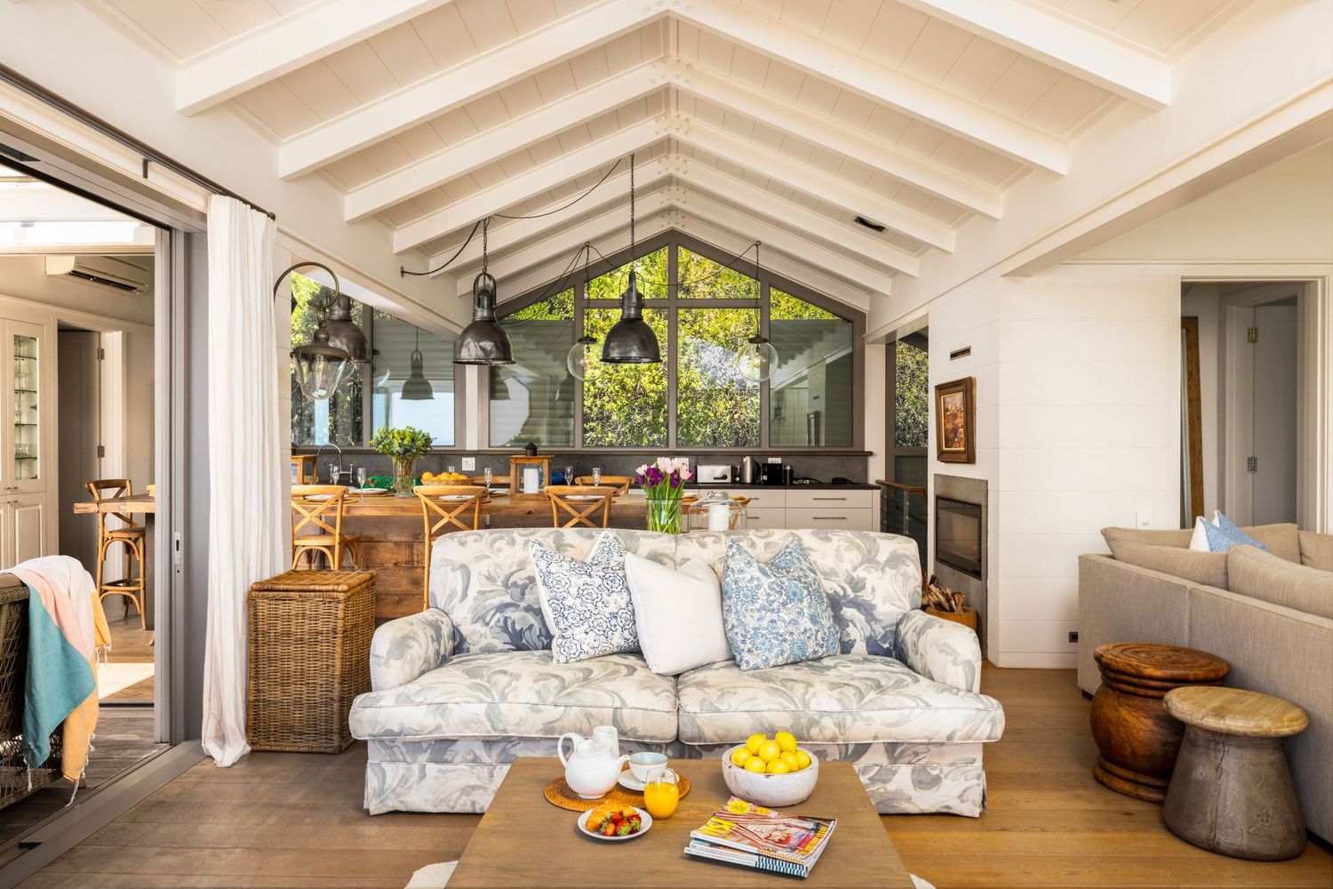 Bright coastal living room with vaulted ceiling, floral sofa, and large windows overlooking tropical greenery.