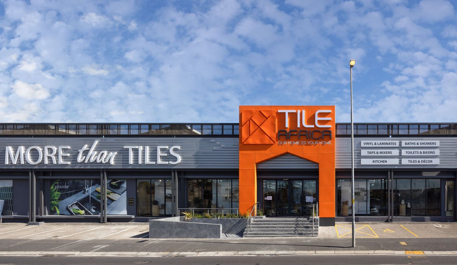 Strip mall exterior with orange and gray signage under blue sky with white clouds.