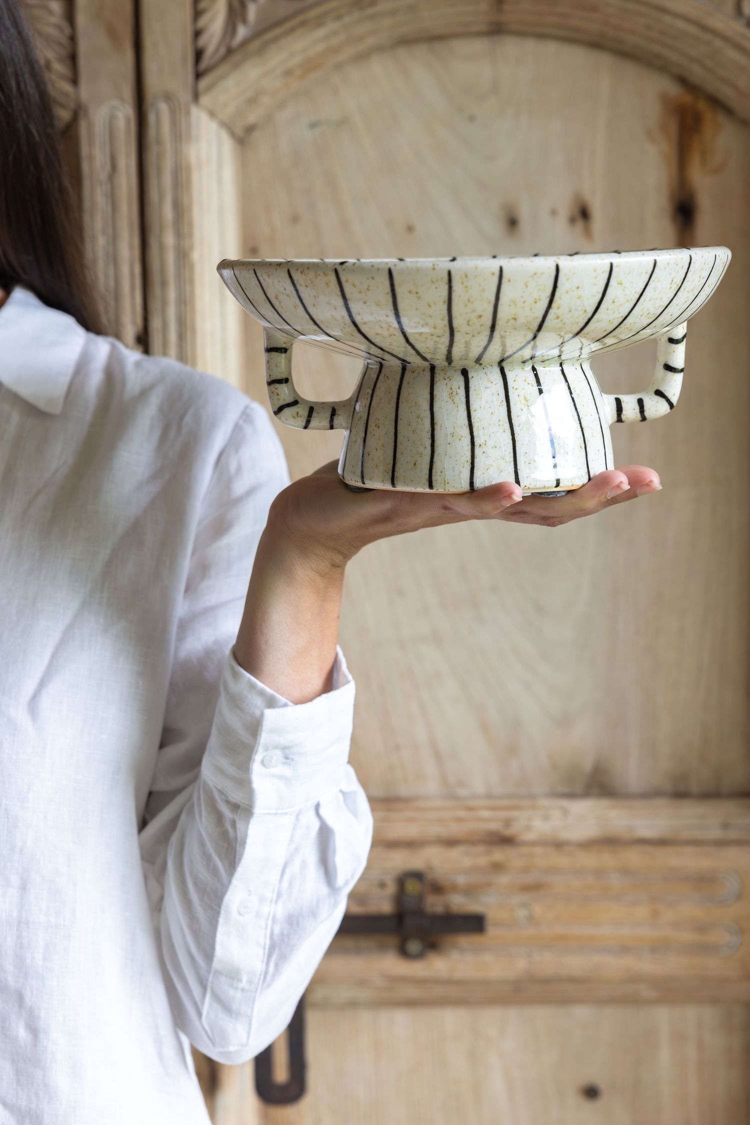 A sequence showing hands in white sleeves placing a ceramic striped bowl onto a wooden surface in multiple steps.