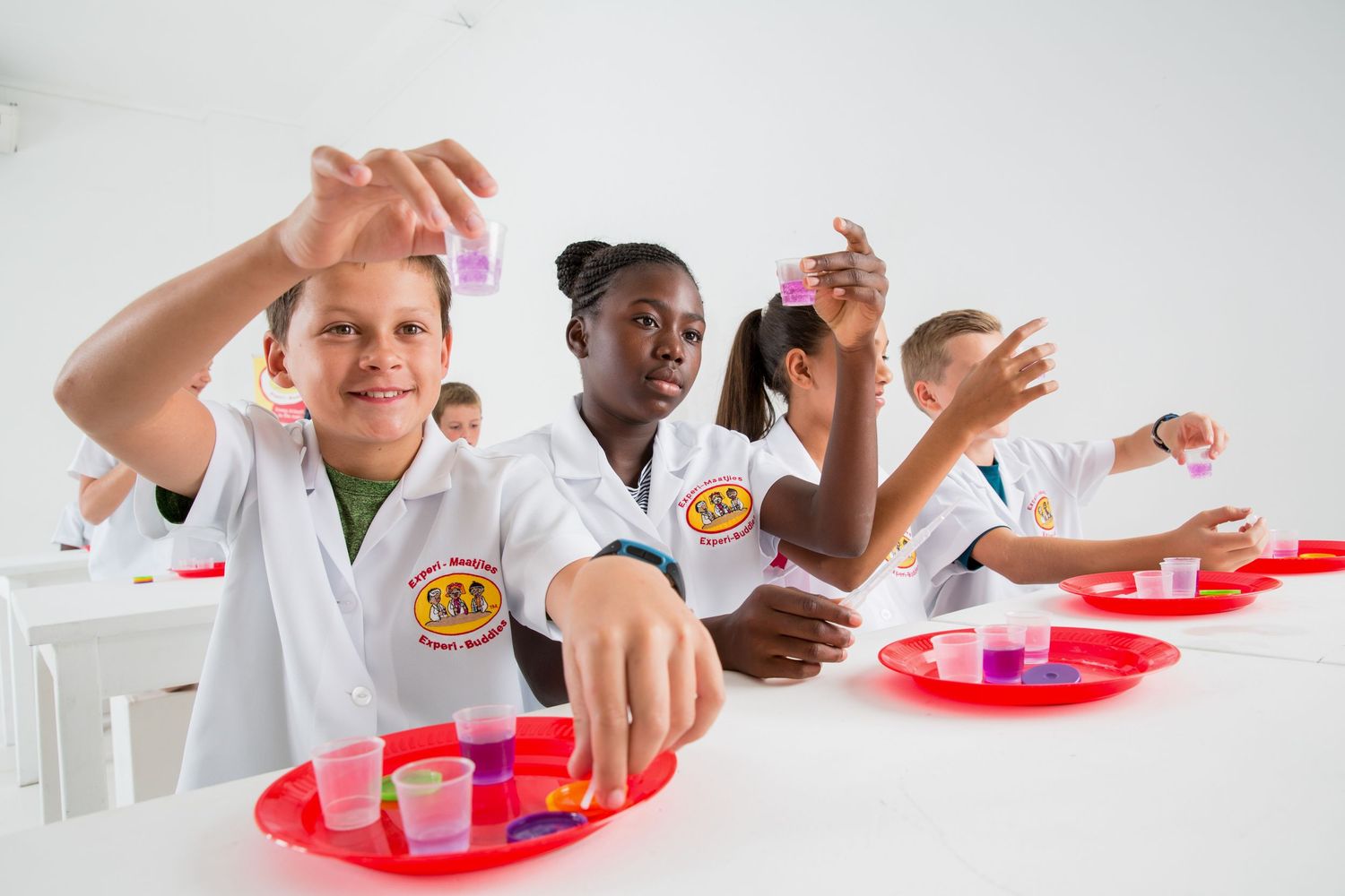 Students in white lab coats react excitedly during science experiment.