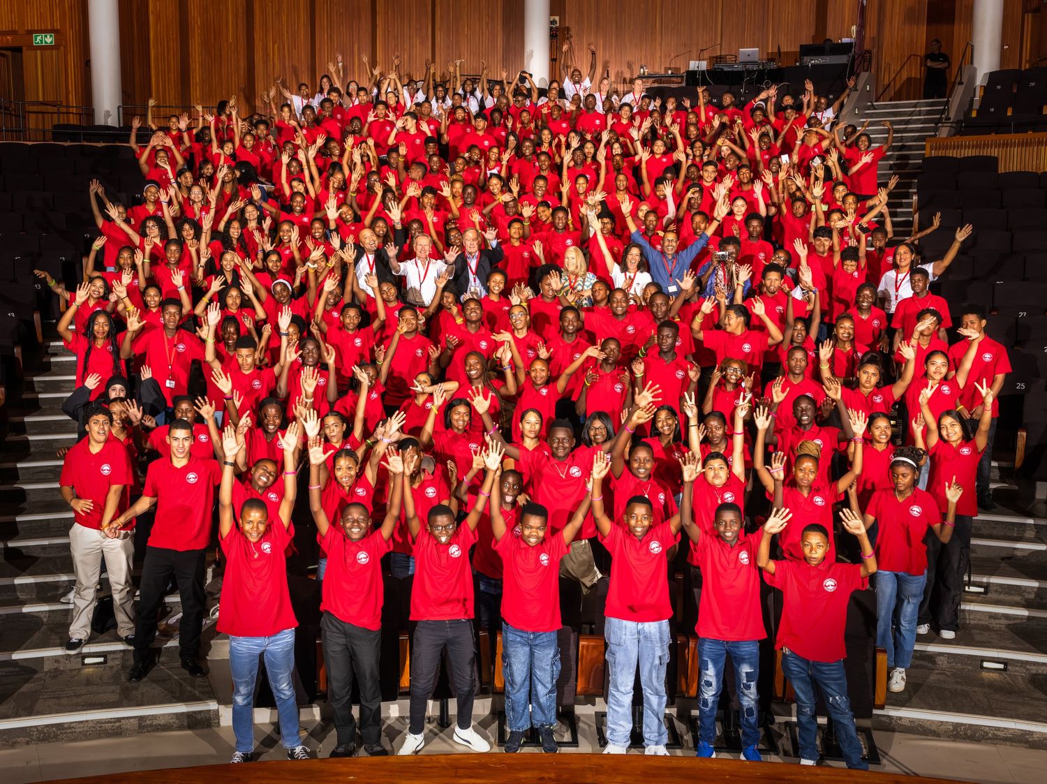 A panoramic view of a large group wearing red shirts posed on bleacher-style steps for a group photo.
