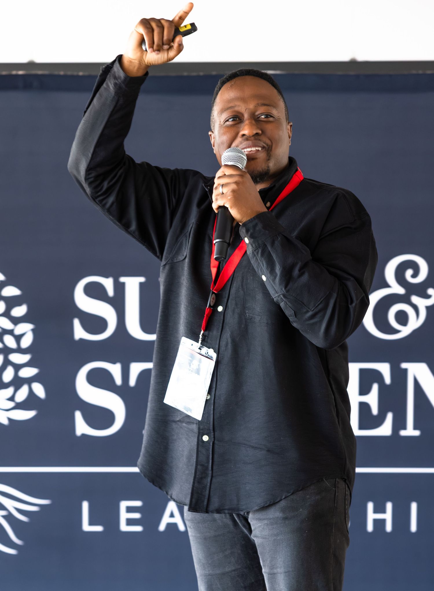 Speaker gestures while presenting at a leadership event with corporate branding visible in the background.