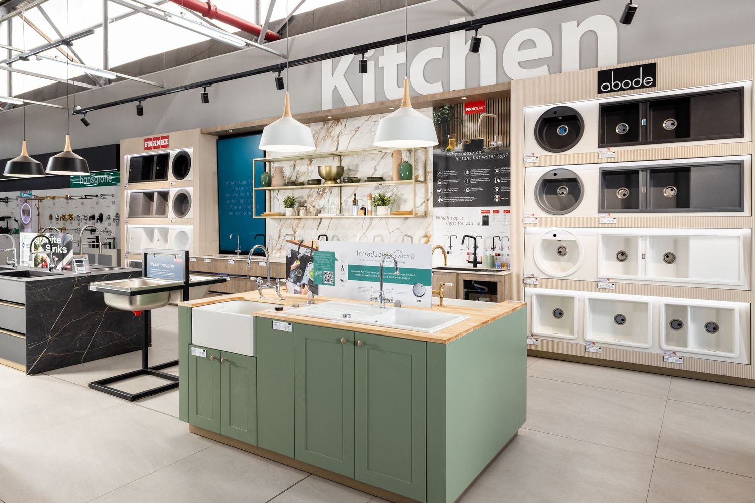 Modern kitchen showroom displays sleek sage green cabinets and white countertops with pendant lighting and appliances.