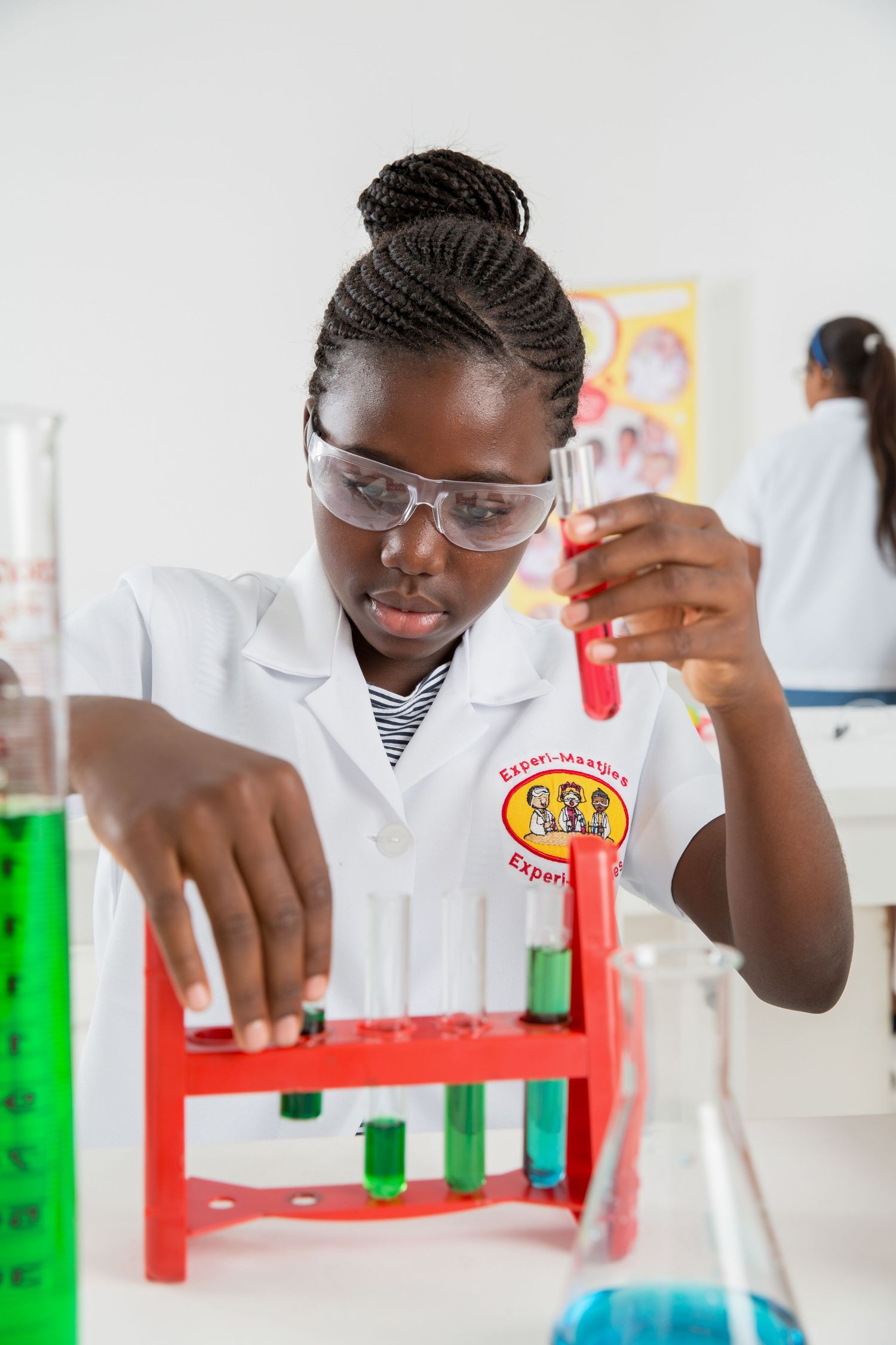Student wearing safety gear conducts experiment with colored solutions in test tubes.