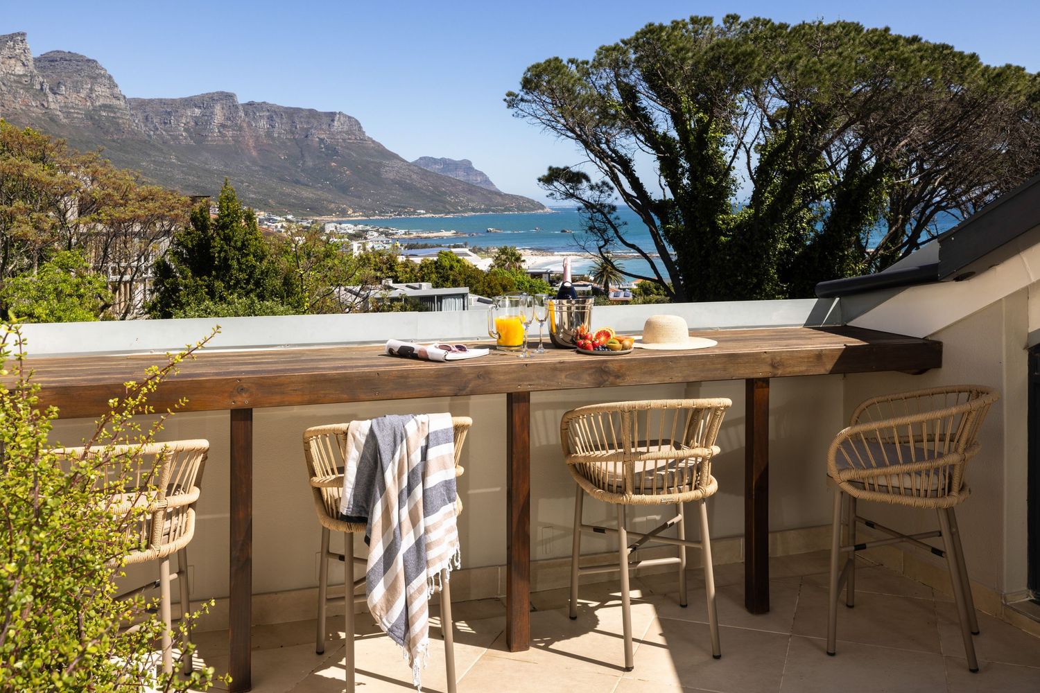 Outdoor bar area with ocean and mountain views featuring rattan bar stools and a drink setup on the counter.
