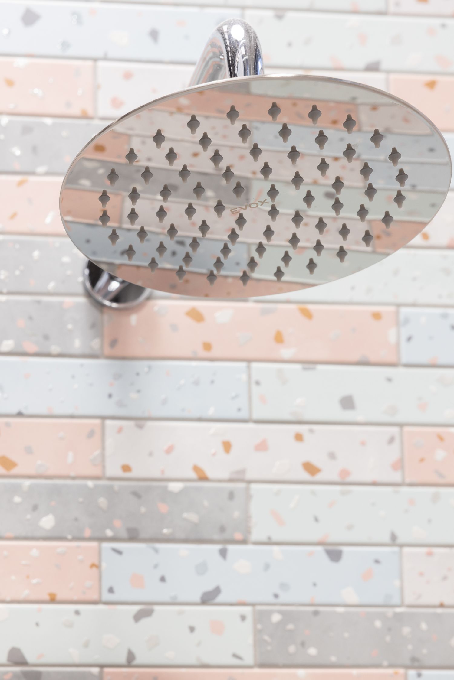 Round chrome rainfall showerhead mounted on pink and white tiled wall.