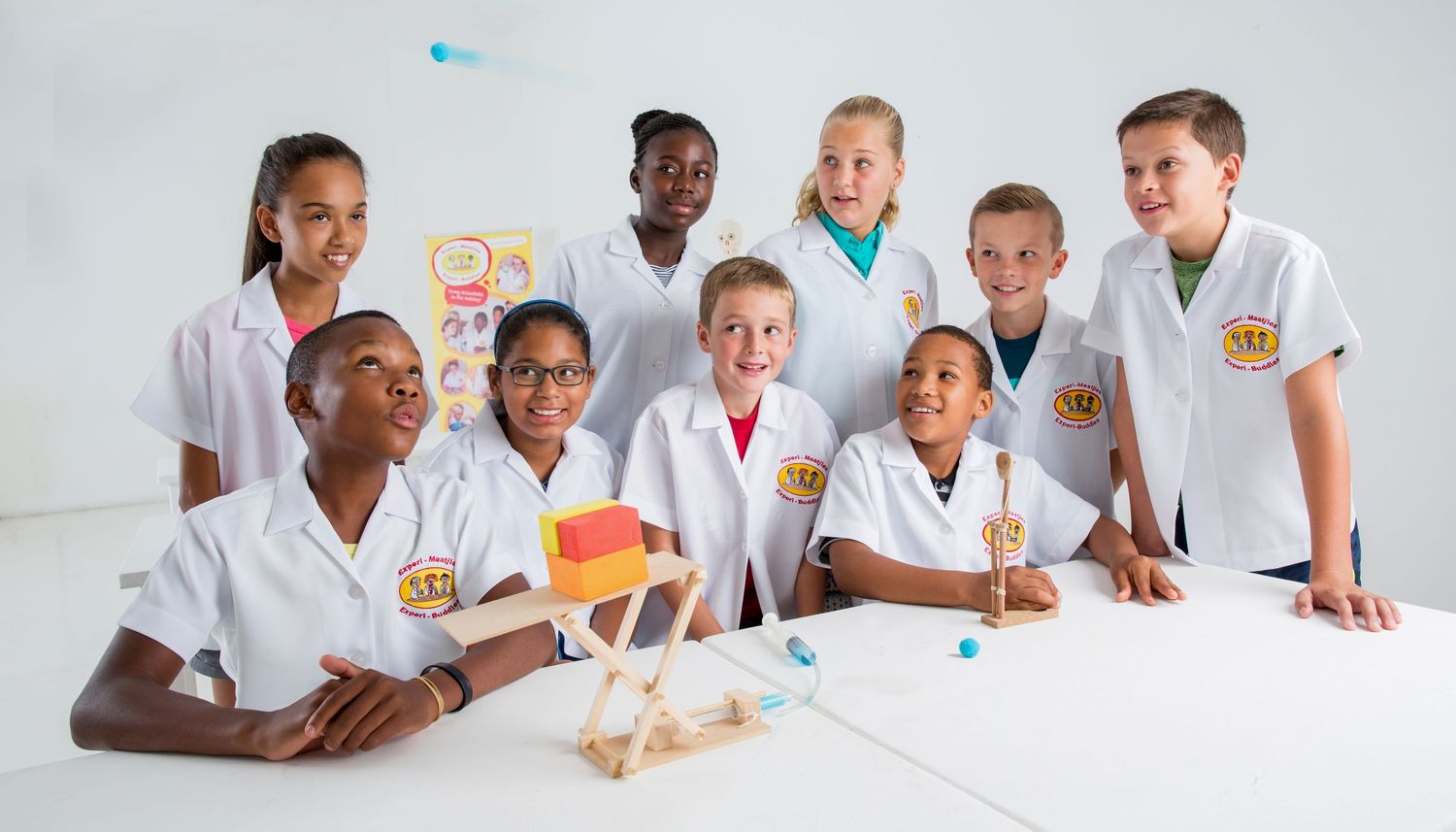 Group of students in white lab coats gather around table examining science project.