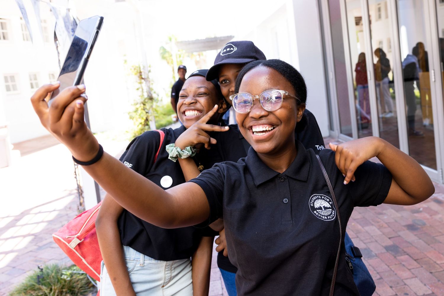 Students take cheerful selfie together outside building wearing matching uniforms.