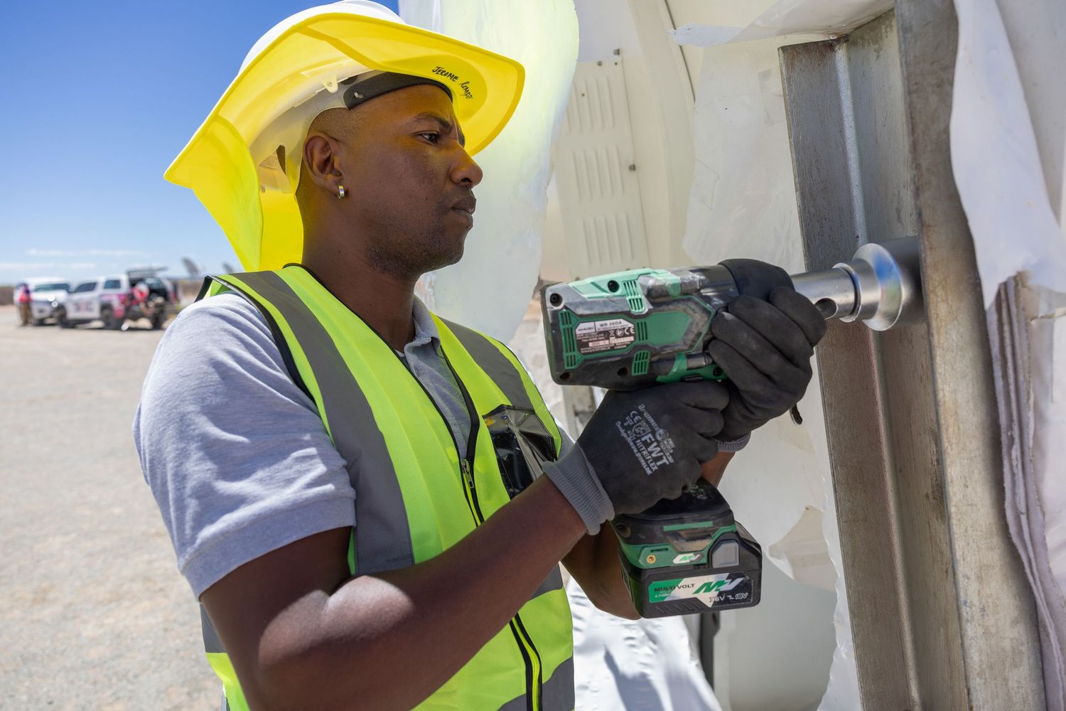 Construction worker in safety gear using power tool on wall at worksite.