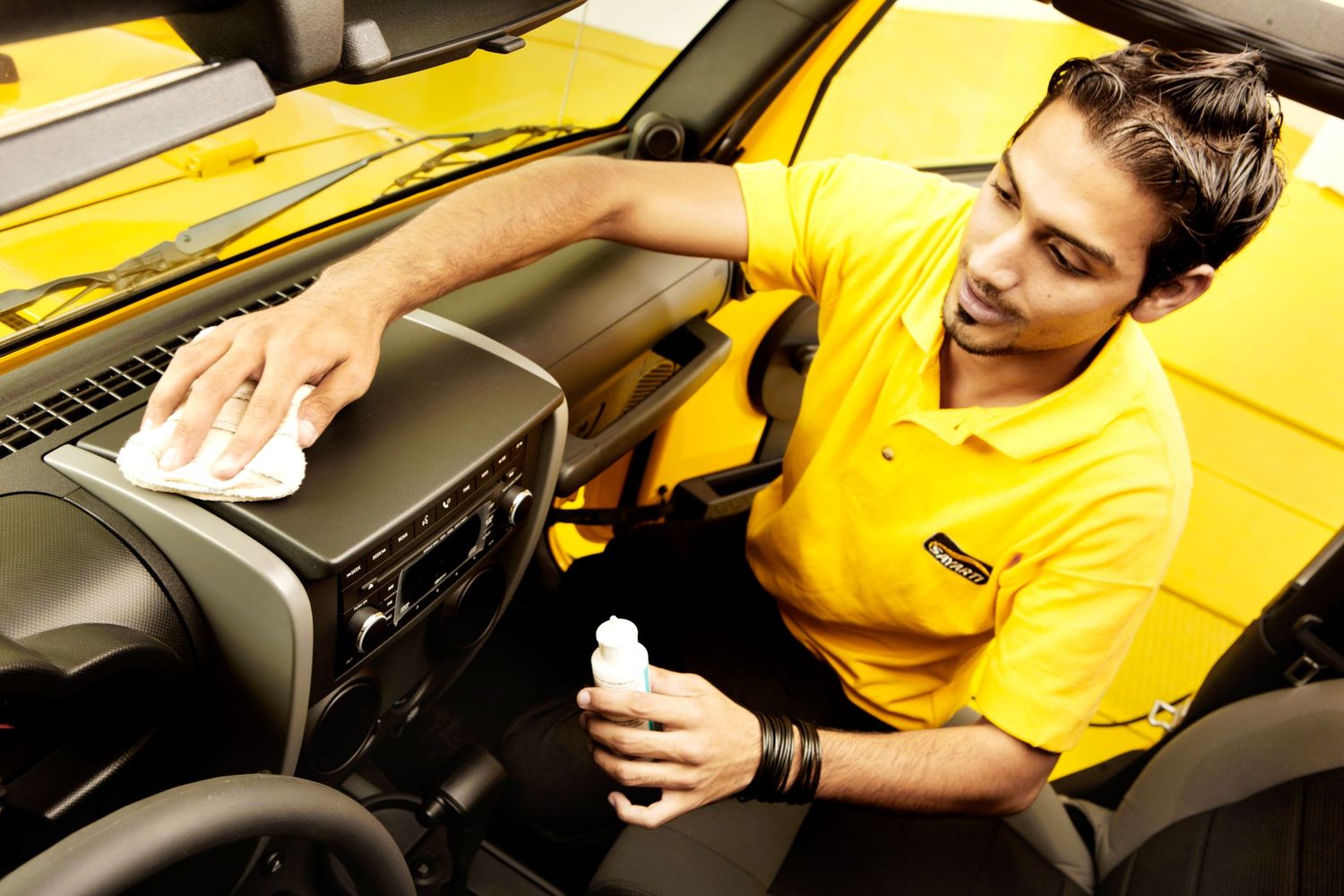 Auto detailing technician cleaning interior dashboard of yellow vehicle.
