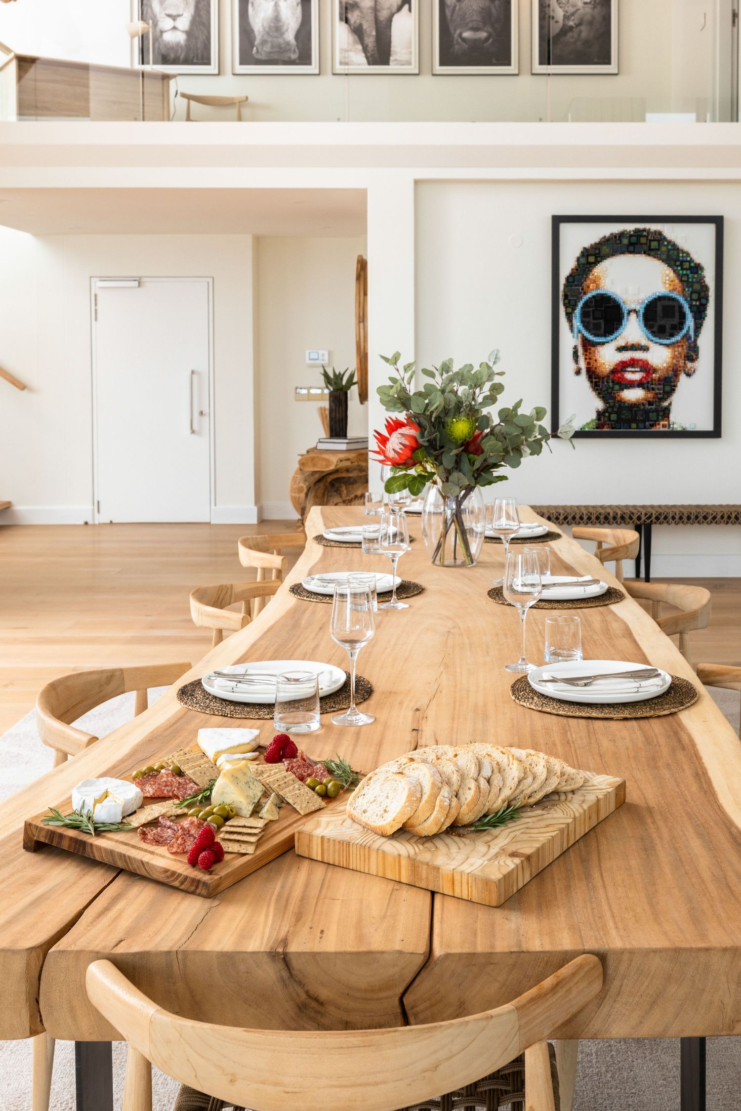 Wooden dining table set with charcuterie boards and appetizers in a modern, well-lit dining space.