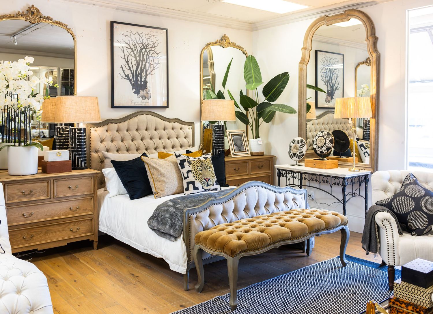 Elegant master bedroom with tufted headboard, gold mirror, and neutral decor showcases luxurious design elements.