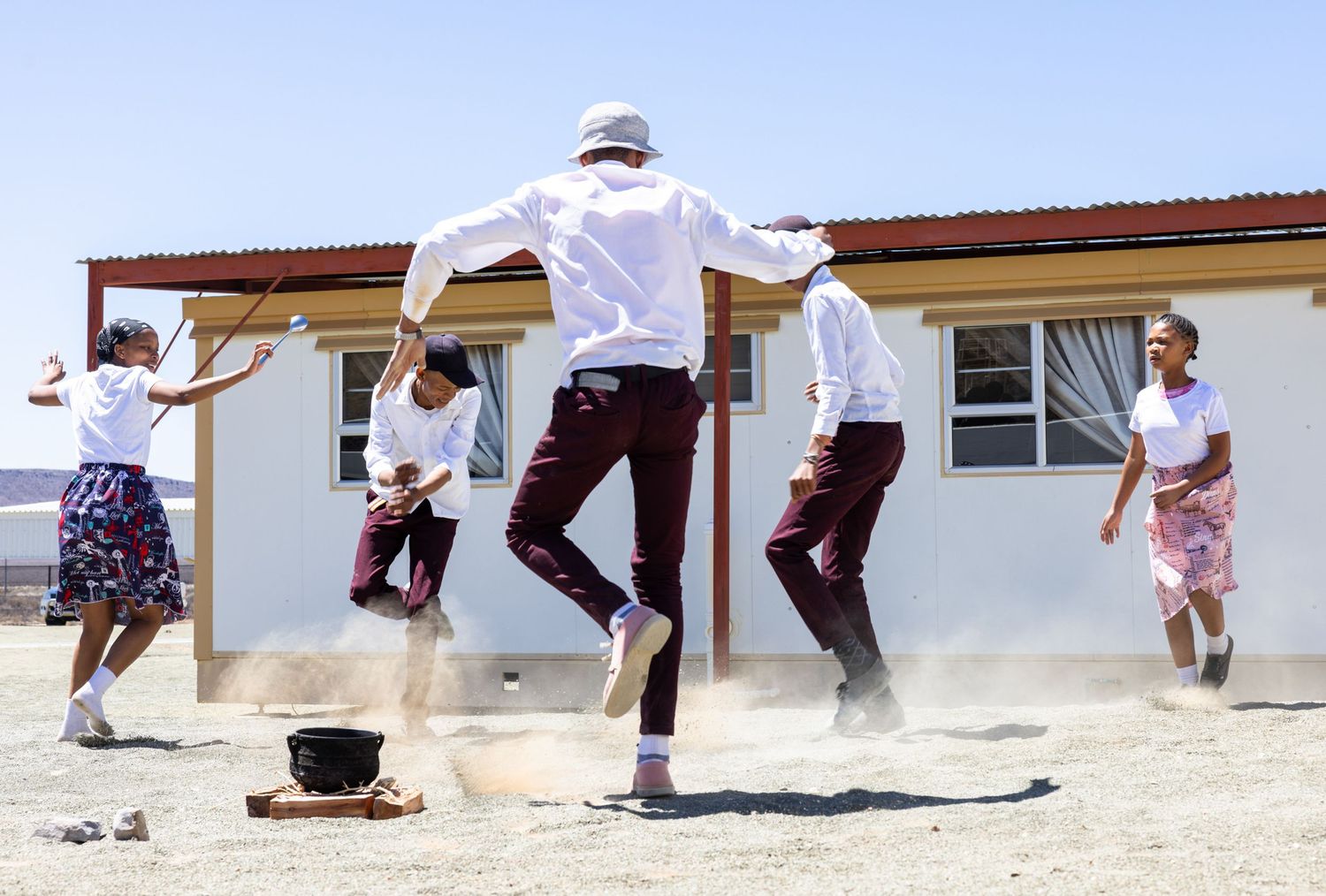 Group of people jumping in synchronized motion outside desert building.