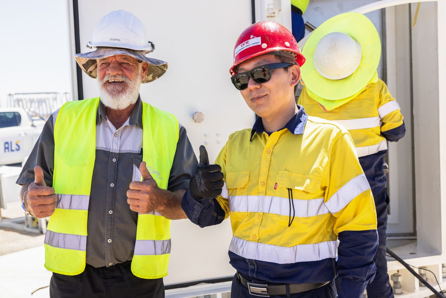Workers in high-visibility gear and hard hats inspect equipment at an outdoor facility.